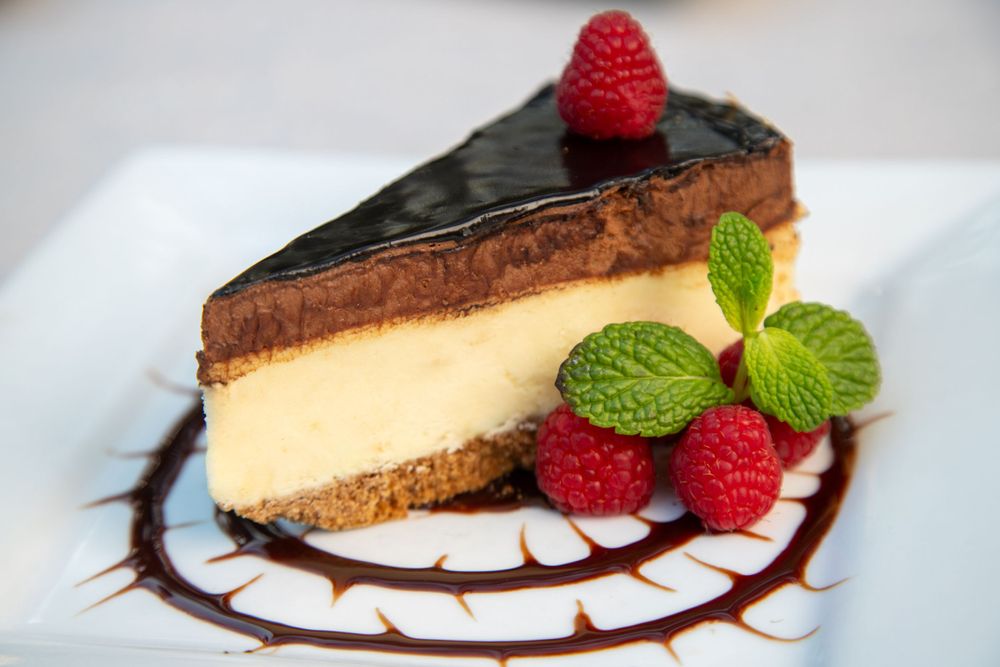 Elegant chocolate cheesecake slice garnished with fresh raspberries and mint on a decorated plate.