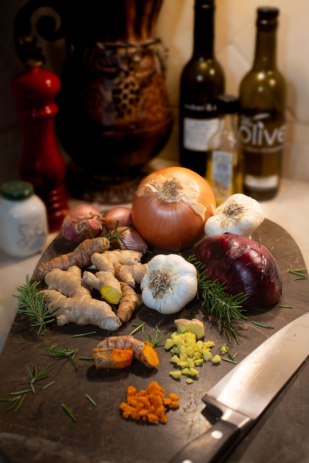 Fresh cooking ingredients including onions, garlic, ginger and spices arranged on a dark cutting board.