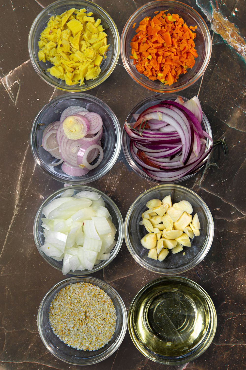 Organized prep bowls containing chopped vegetables including carrots, onions, garlic and seasonings.