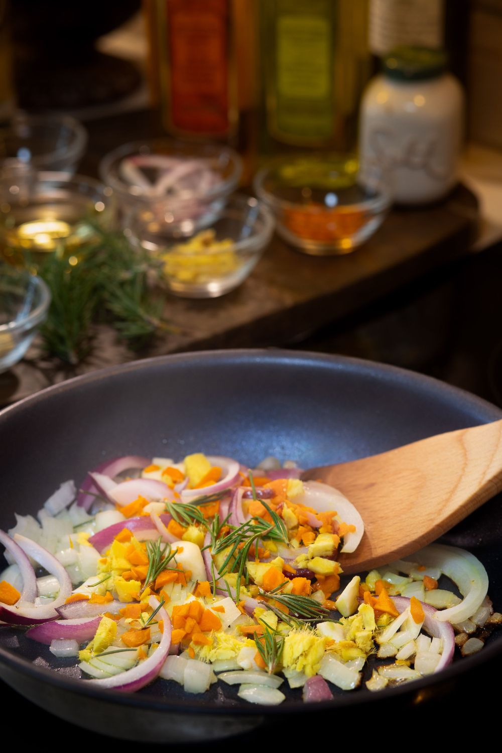 Fresh vegetables being sautéed in a pan with a wooden spoon.