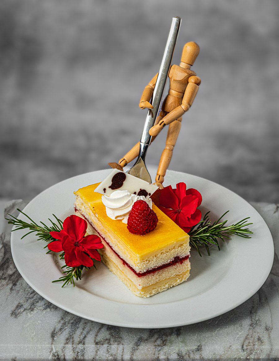 Wooden artist mannequin serving a decorated dessert slice with strawberries and flowers on white plate.