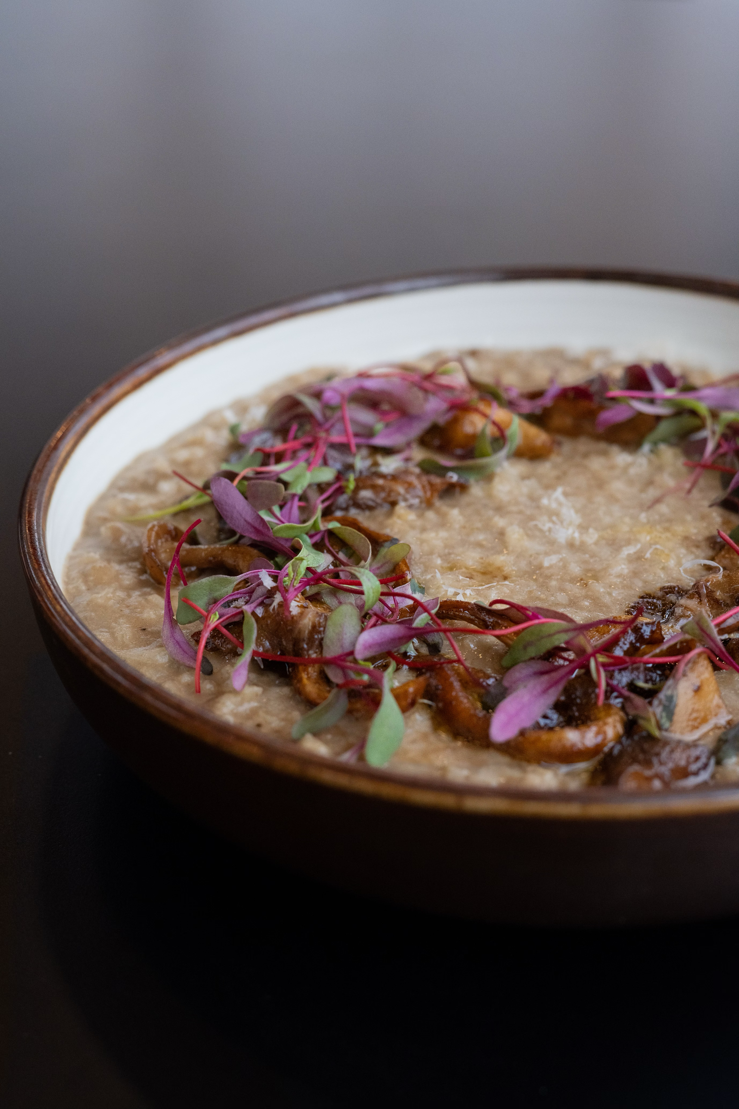 Rustic bowl of risotto garnished with purple microgreens and mushrooms.