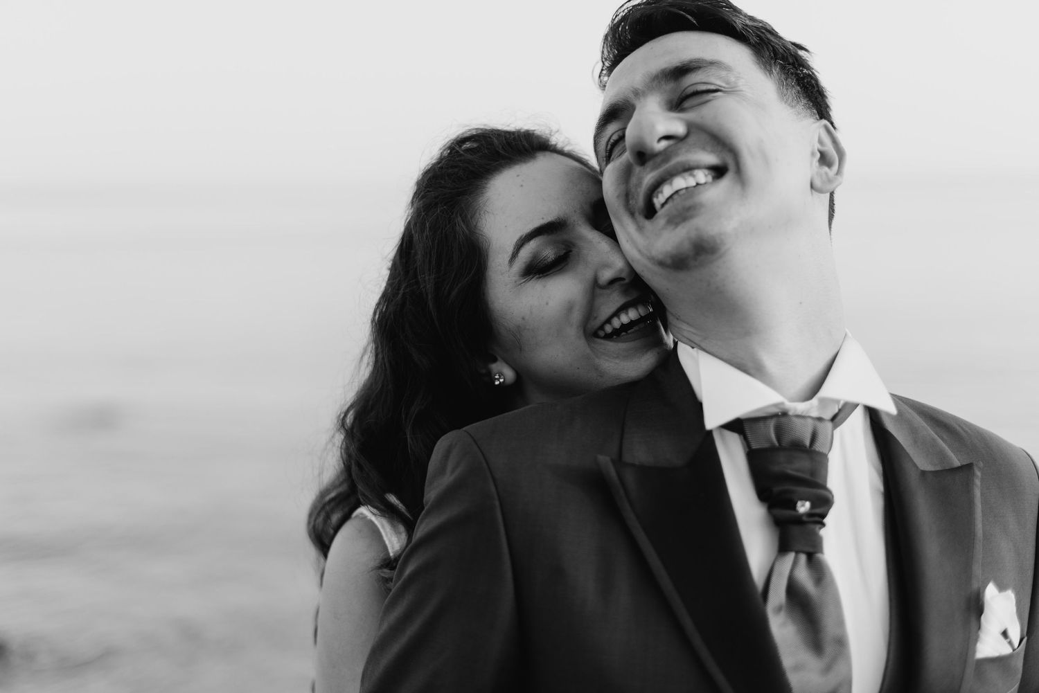 A romantic black and white portrait of a couple laughing together on their wedding day.
