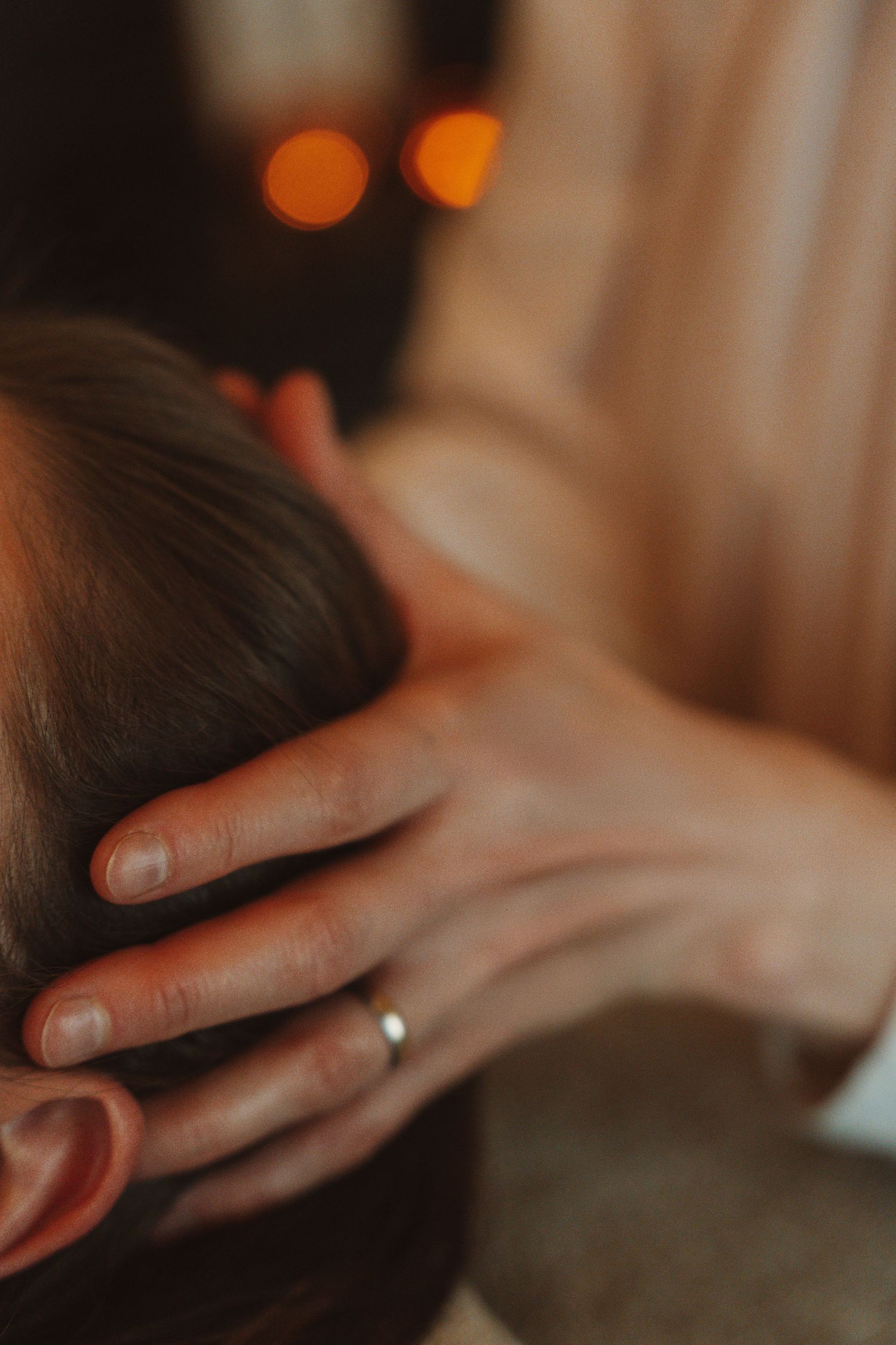 Close up of a gentle hand touching hair with a ring glinting in warm ambient lighting.