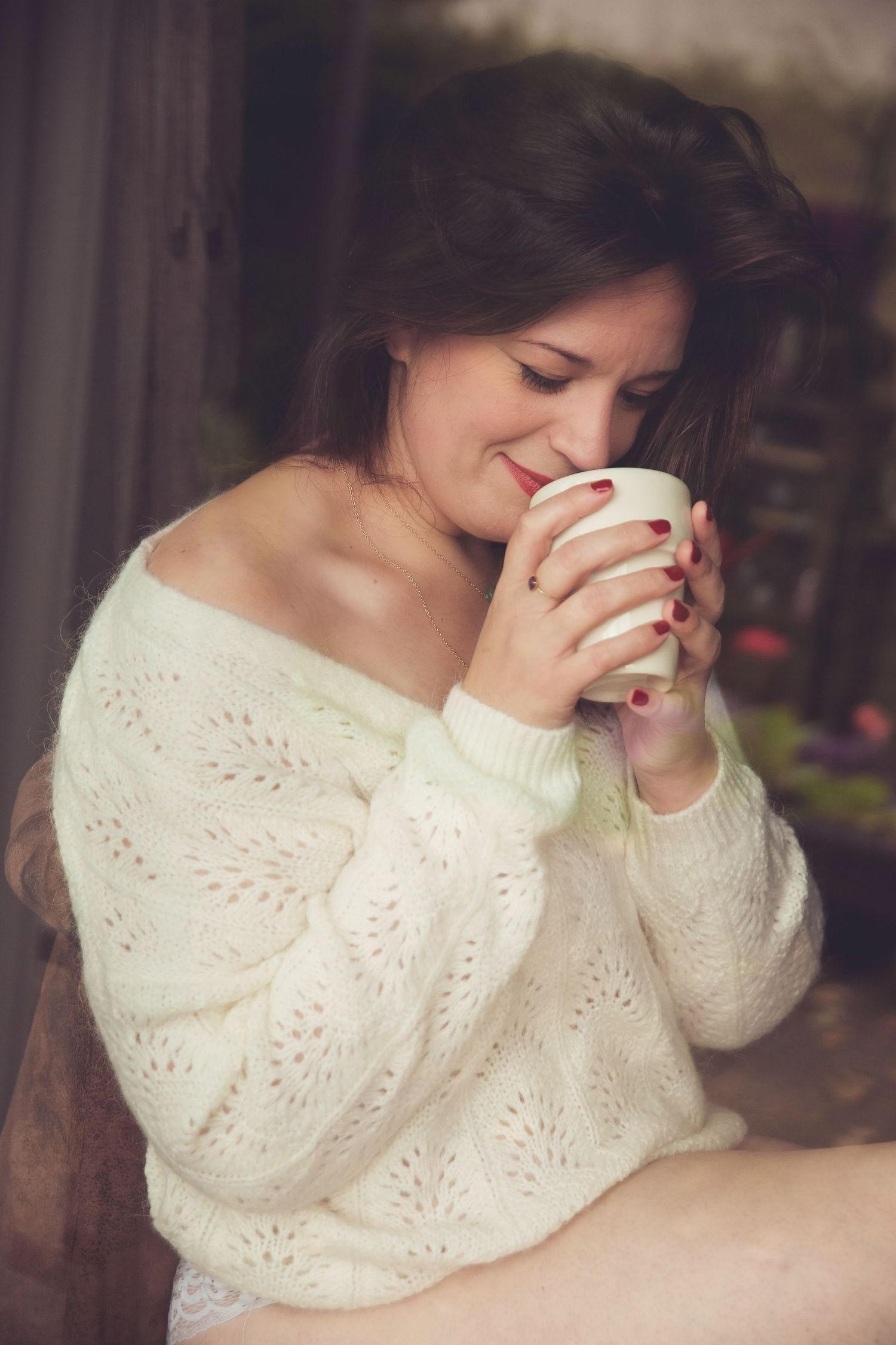 Cozy portrait of person in cream sweater enjoying hot beverage by window.