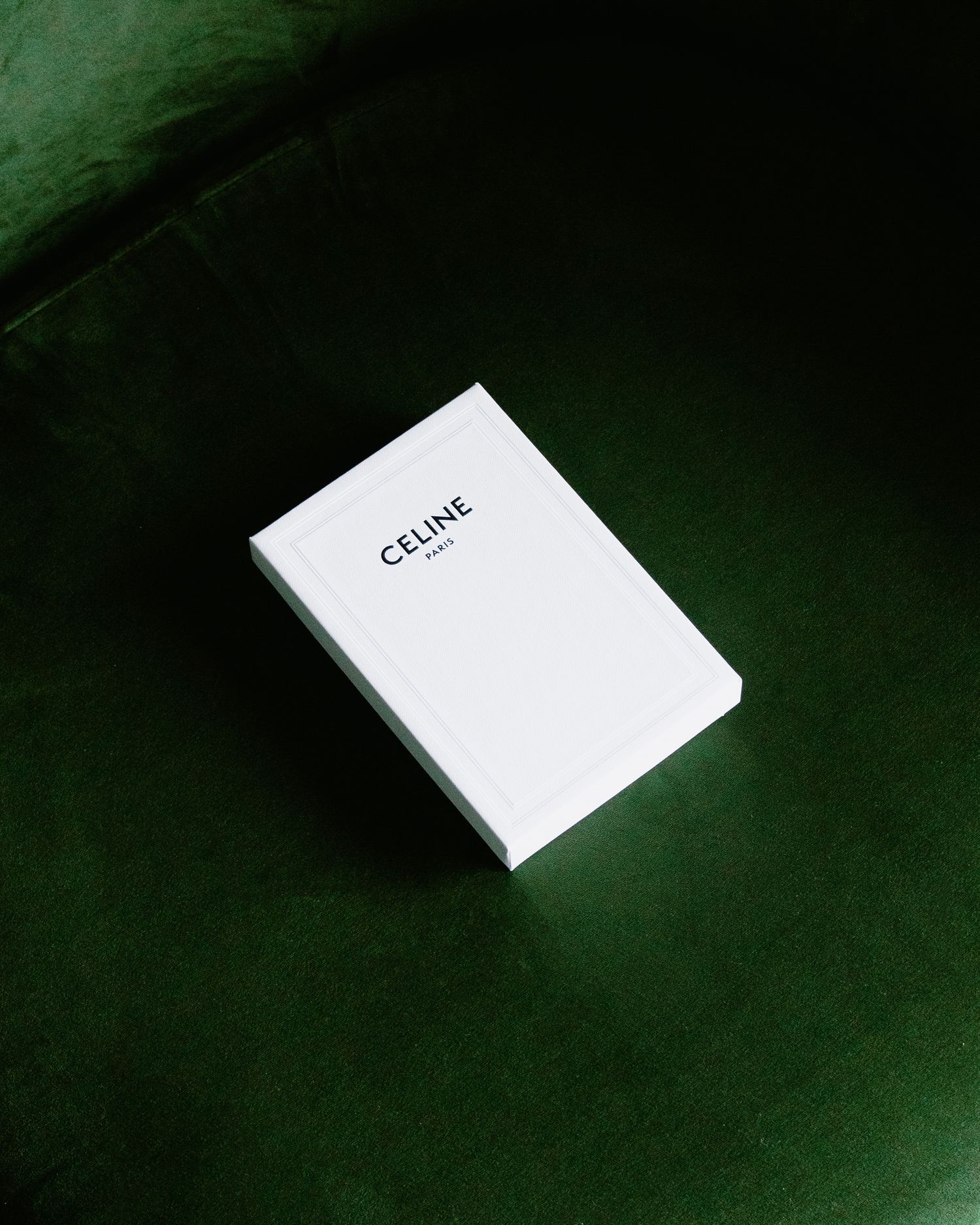 Minimalist product shot of white Celine box on dark green velvet surface.