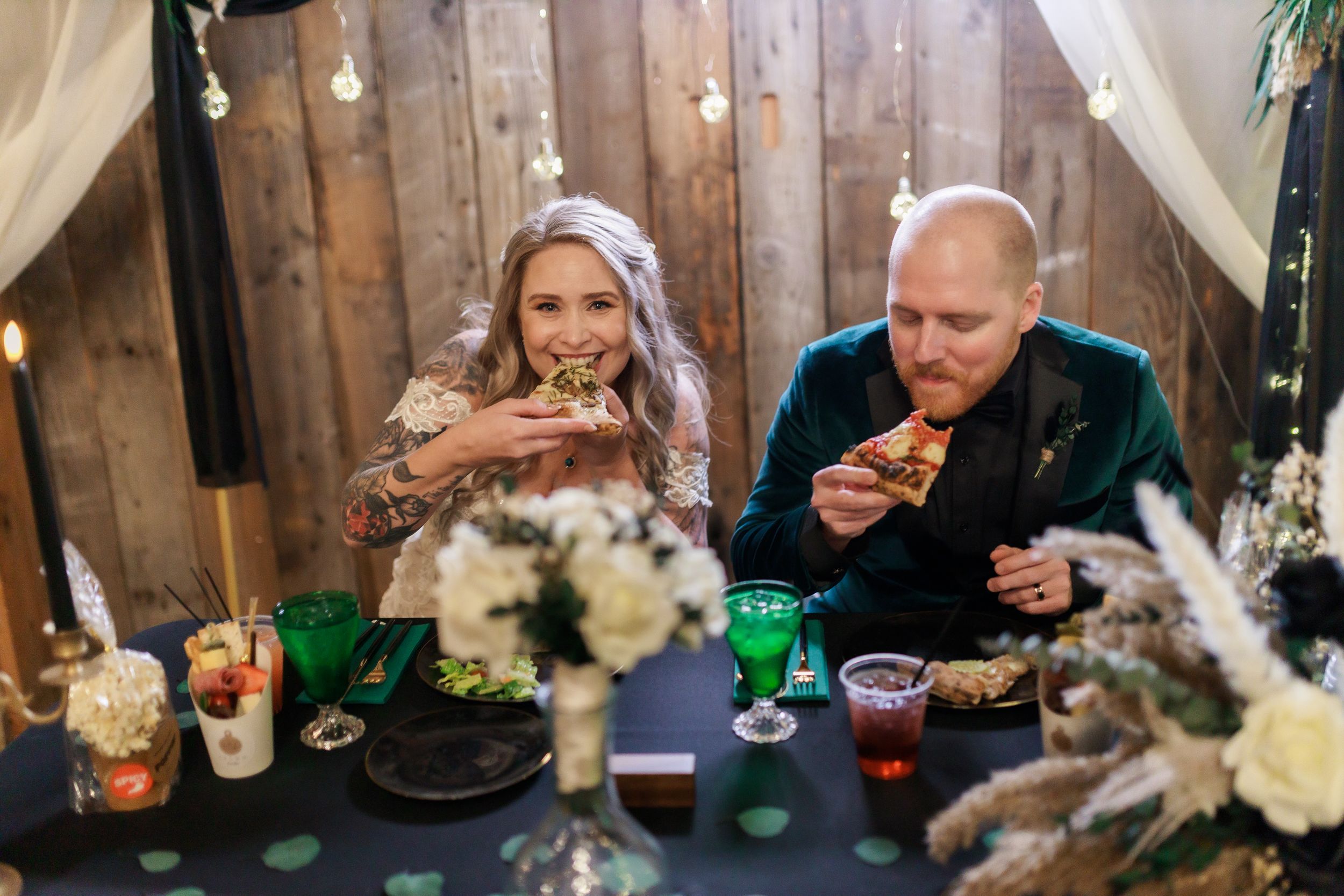Couple enjoying pizza at wedding reception with green glassware and floral centerpieces captured by Michigan wedding photographer.