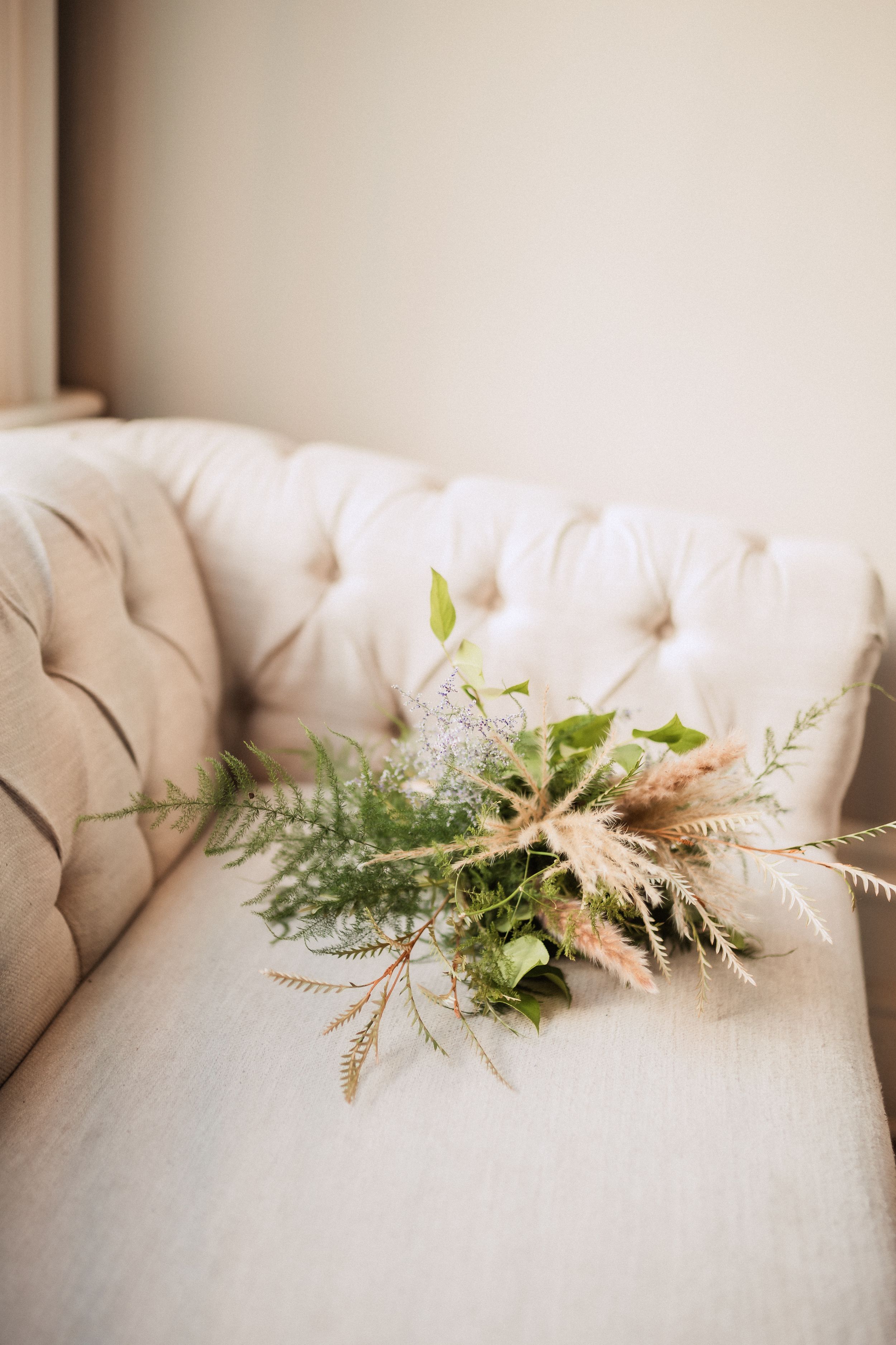 Rustic dried floral arrangement with pampas grass and greenery rests on a cream tufted sofa.