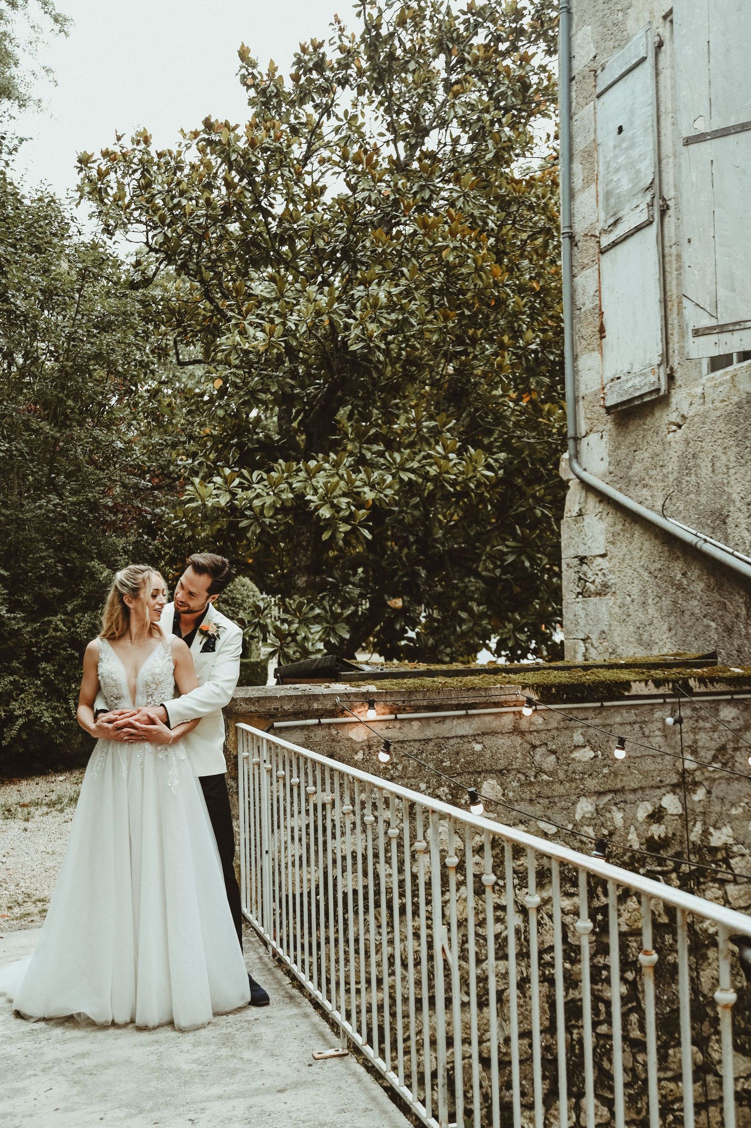 Romantic wedding couple embracing on stone staircase beside vintage building.