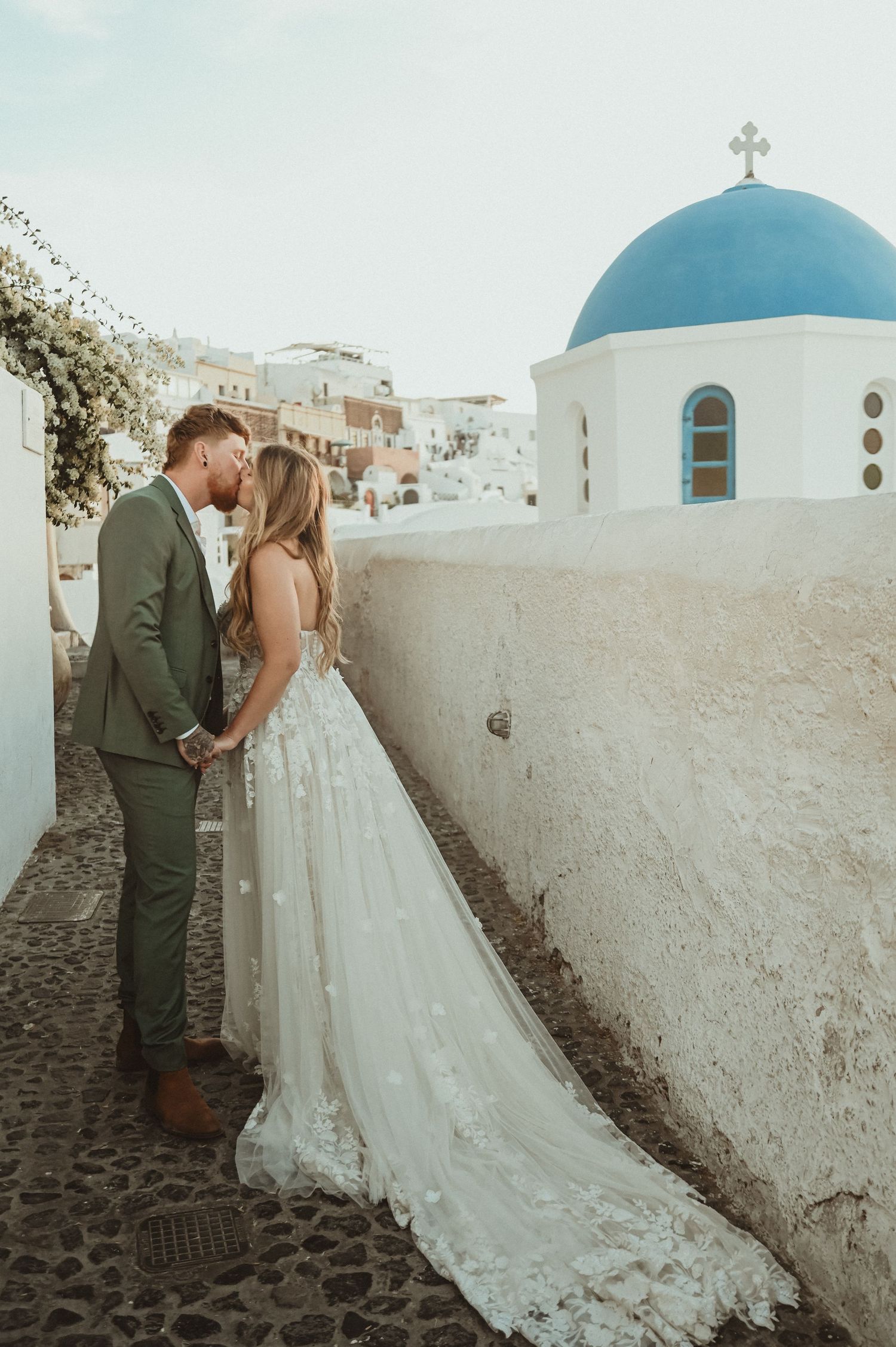 Wedding couple against white Santorini church with blue dome in Greece.