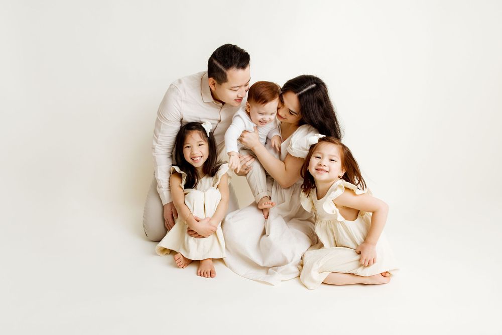 Family sitting on the floor, neutral backdrop during a studio family session, laughing