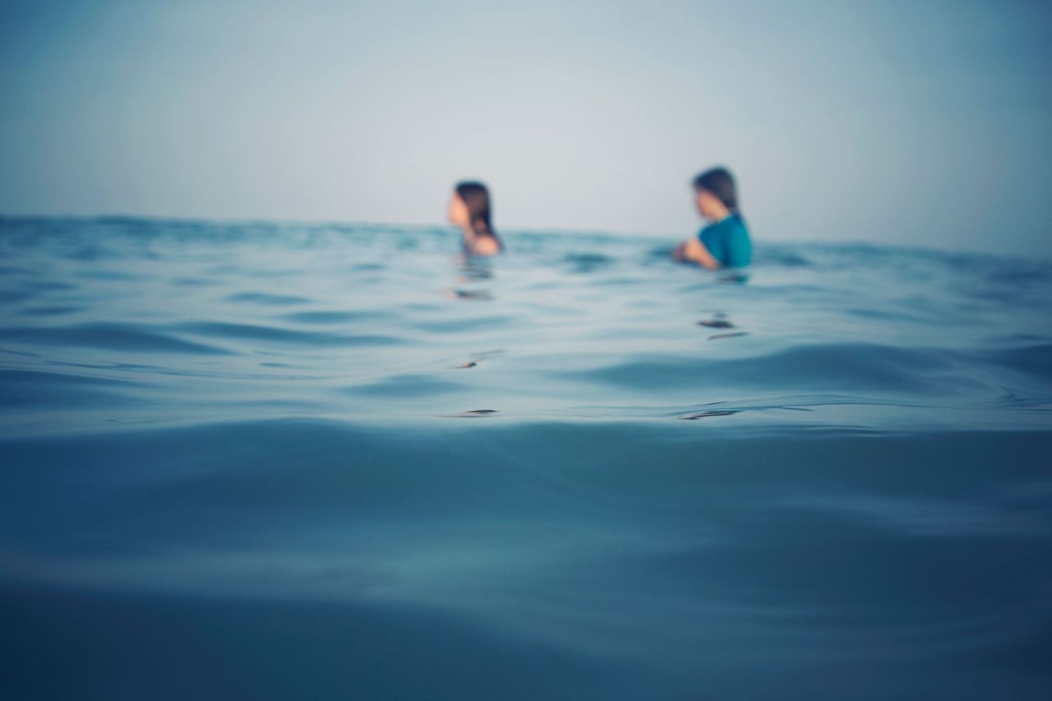 Blurred figures swimming in deep blue ocean waters on a hazy summer day.