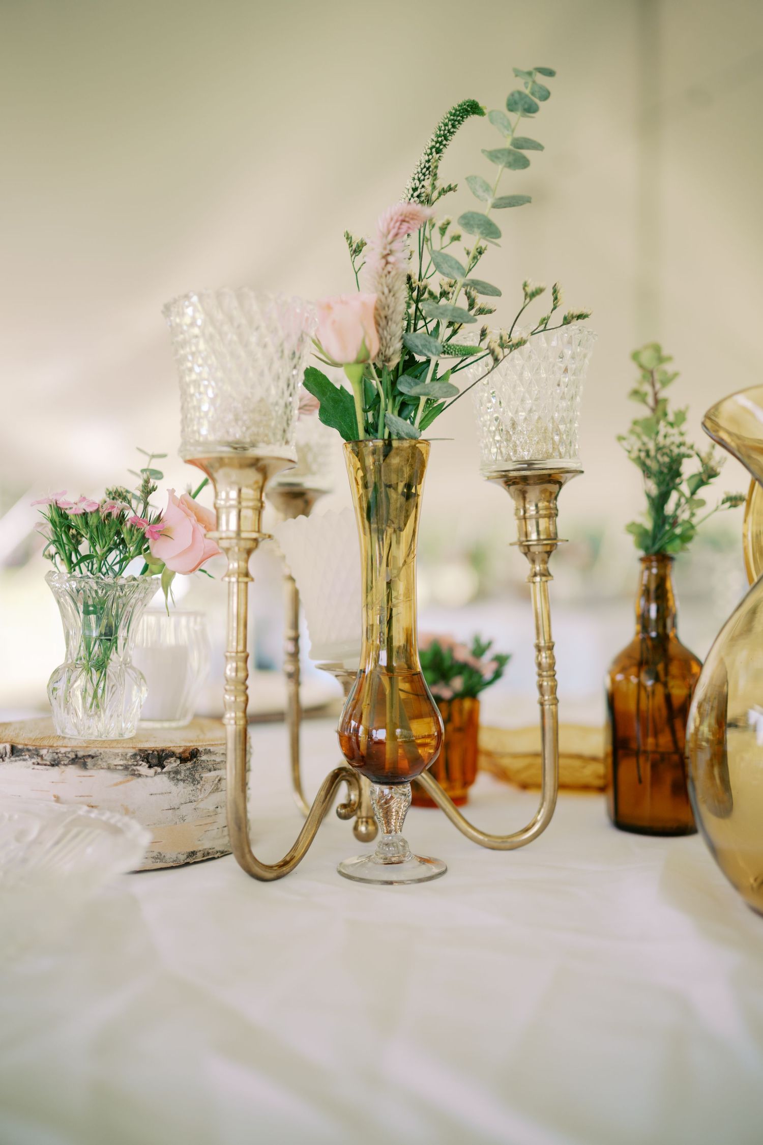 Vintage brass candlesticks and amber glass vases filled with delicate flowers create an elegant table decoration.