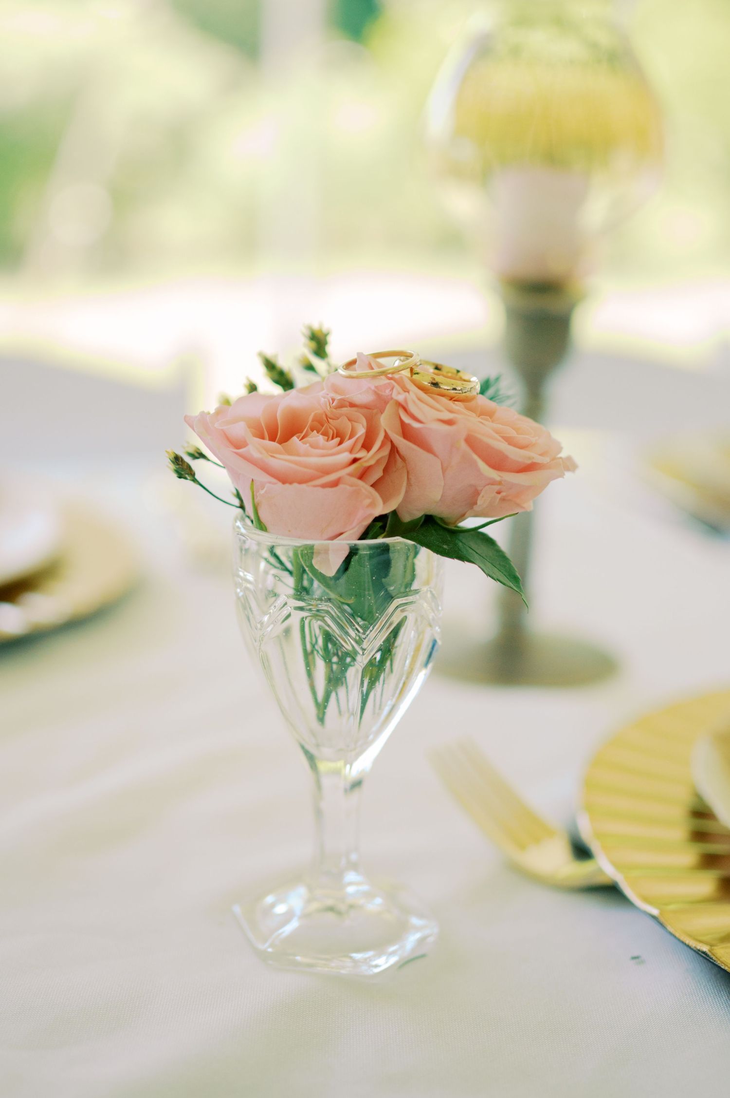 Delicate peach roses arranged in an elegant crystal wine glass centerpiece on a white tablecloth with folded fan decor.