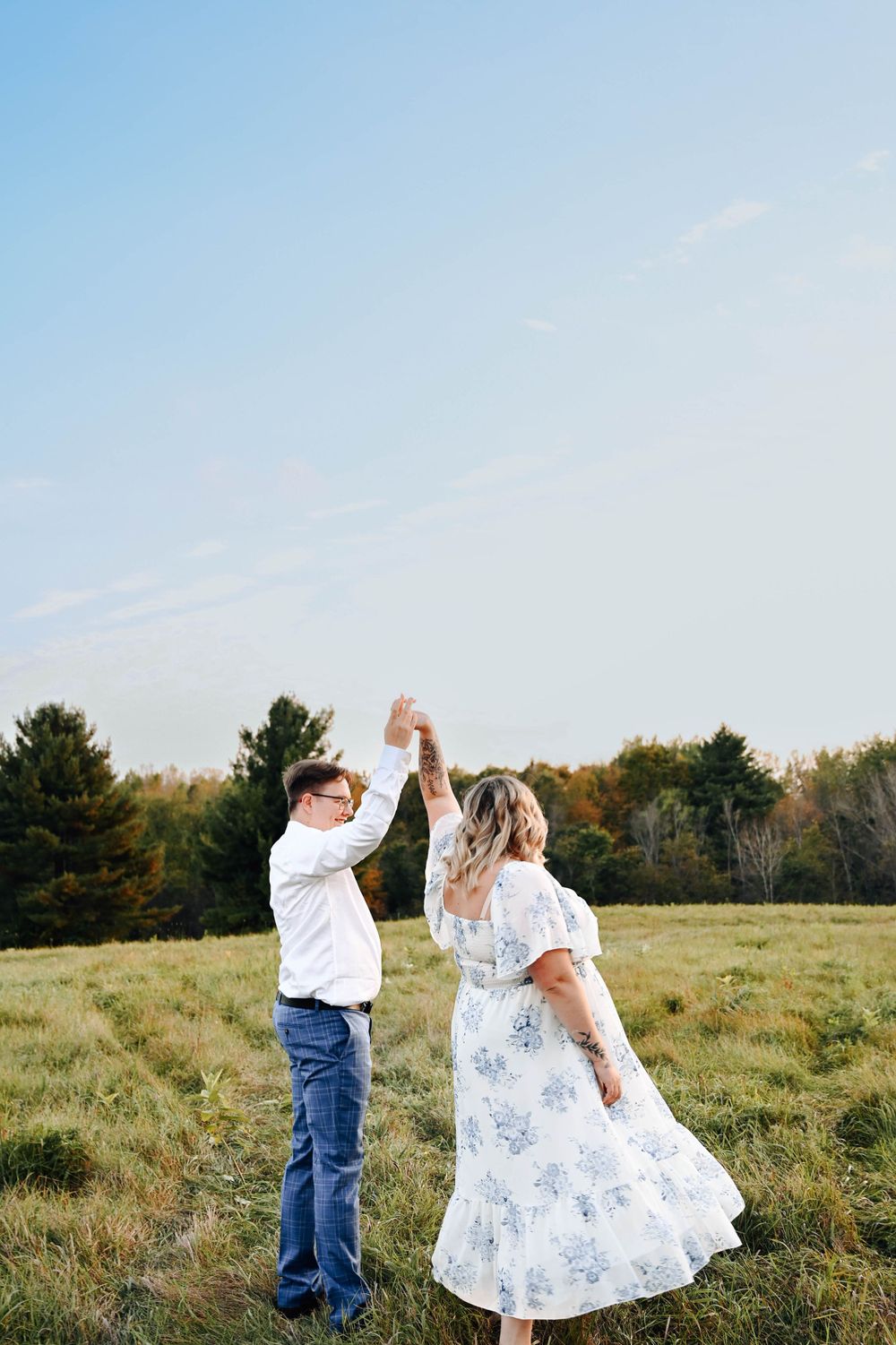A couple dances together in a grassy meadow on an autumn day with trees in the background.