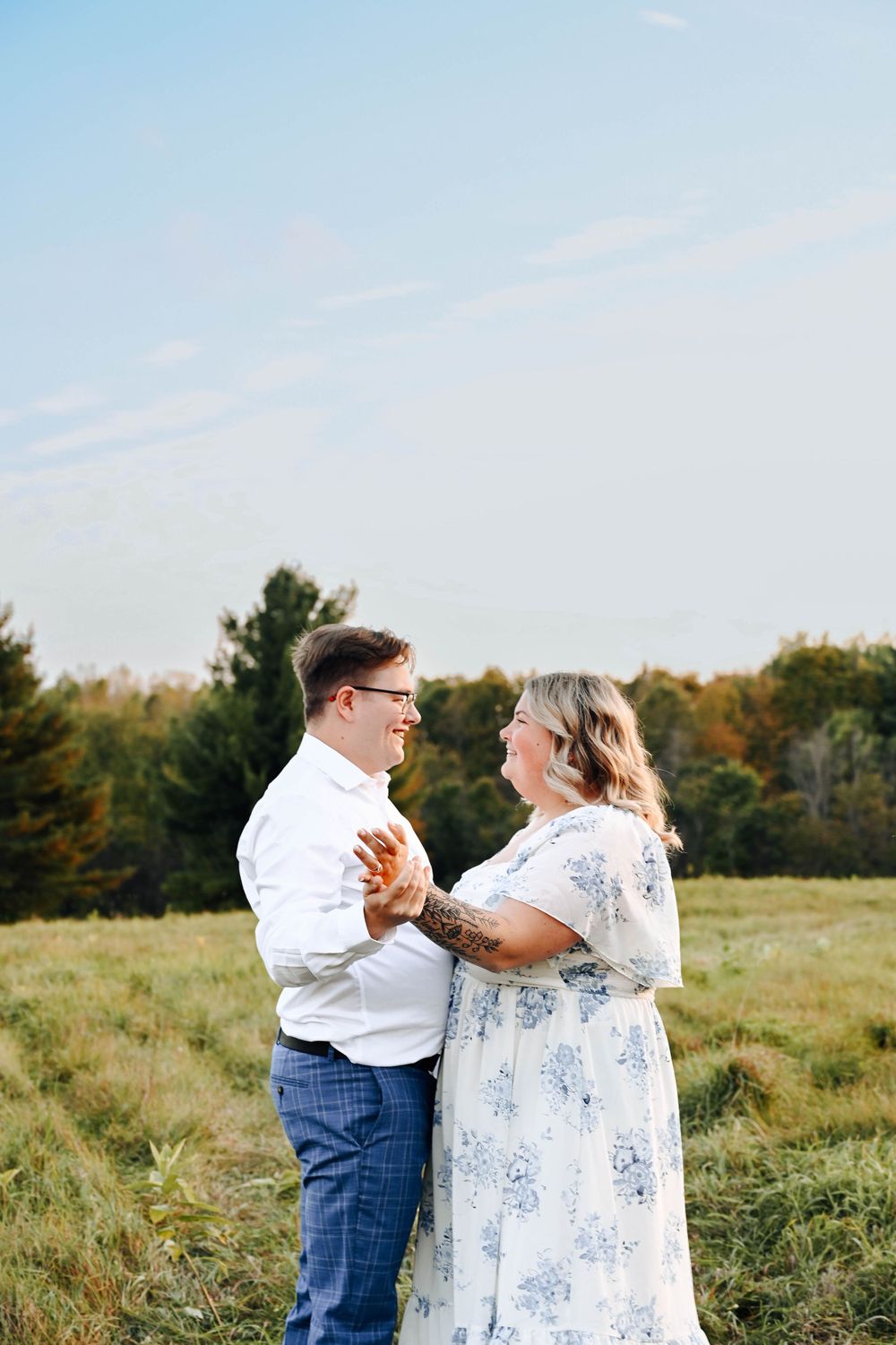 A couple shares a romantic dance together in a sunlit meadow with autumn trees in the background.