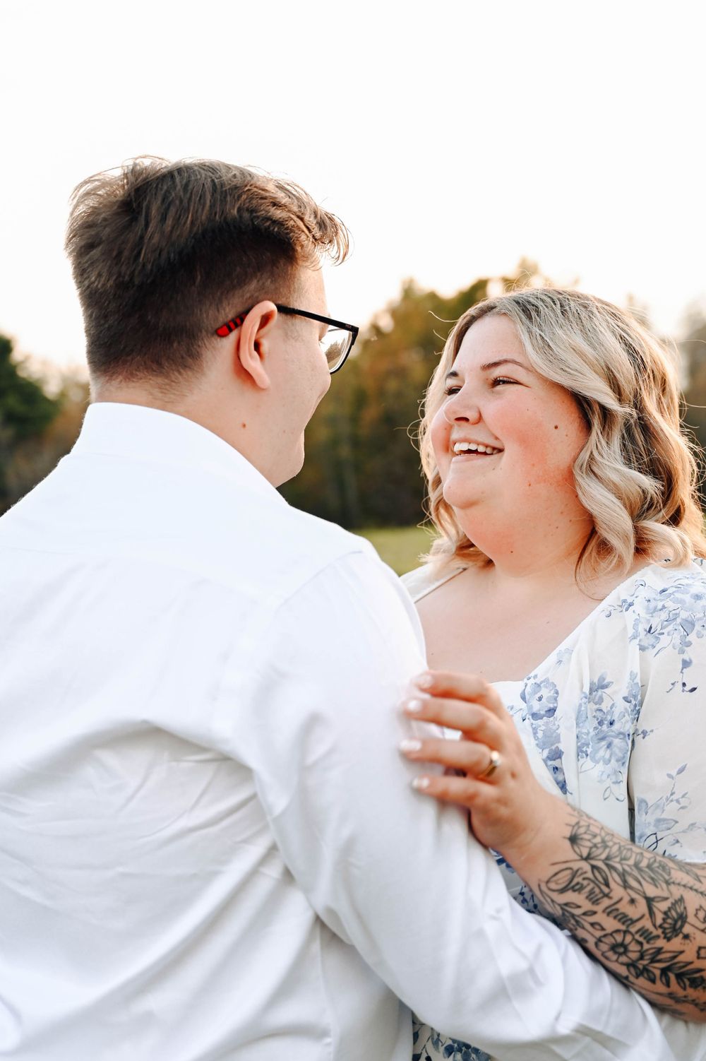 Joyful couple sharing a tender moment while dancing outdoors at golden hour, with one wearing a blue floral dress.
