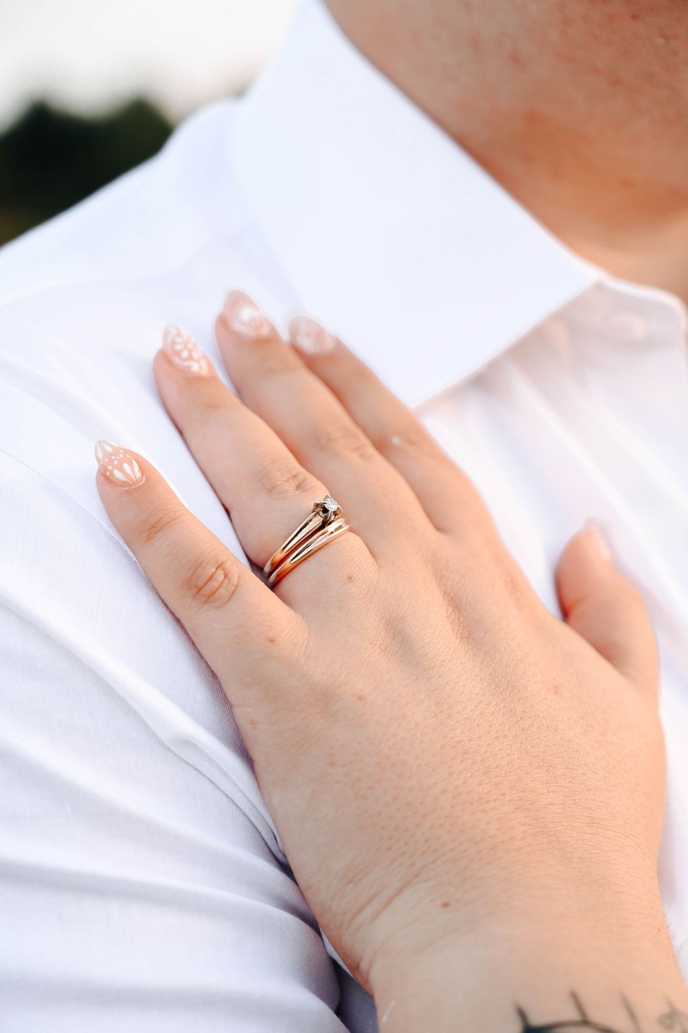 Close-up shot of a hand wearing wedding rings and white lace nail polish design against a white fabric background.