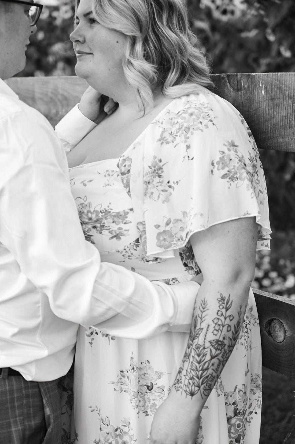 Black and white romantic portrait showing a couple sitting close together, with someone wearing a delicate floral dress.