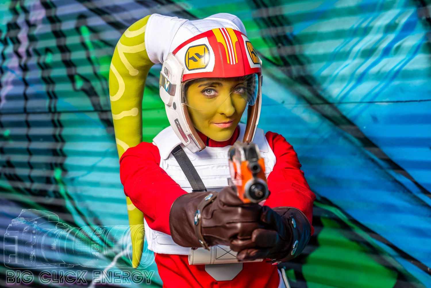 Blaster raised, a Hera Syndulla cosplayer takes aim. Graffiti-covered walls hint at a rebellious urban setting.