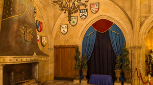 Medieval castle interior with stone walls, heraldic shields, and blue curtained entryway decorated with potted plants.