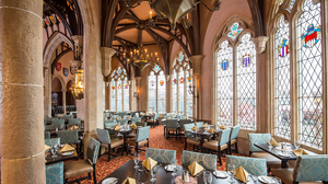 A panoramic view of an ornate gothic church interior with stained glass windows, stone columns and blue upholstered seating.