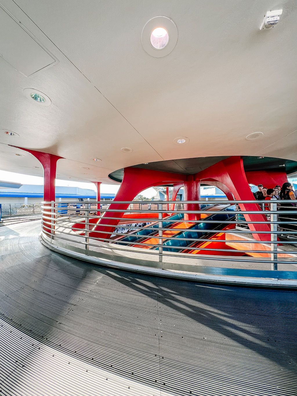 Modern cruise ship deck interior with red support columns and curved railings overlooking the ocean.