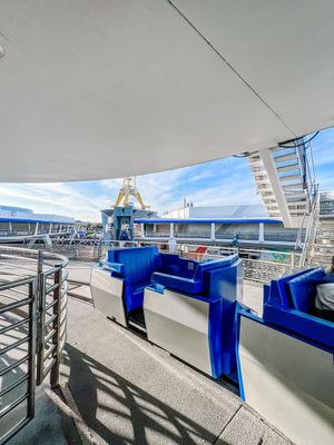 View of blue stadium seats and railings on the deck of a cruise ship under sunny blue skies.