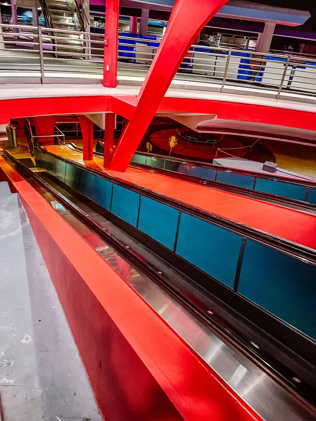 Modern architectural interior with vibrant red beams and turquoise panels featuring an escalator in a multi-level structure.
