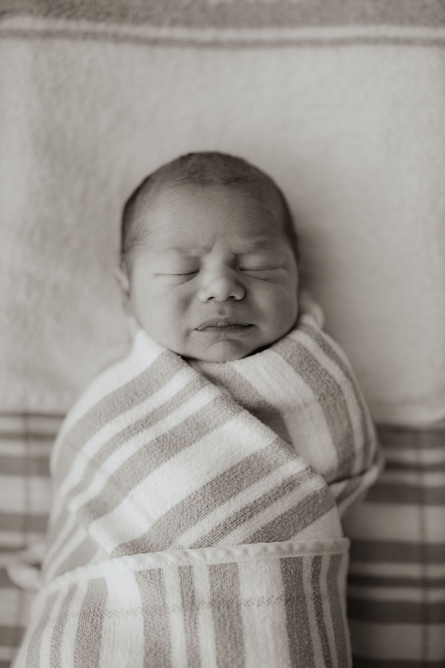 Black and white photo of a sleeping newborn baby swaddled in a striped blanket.
