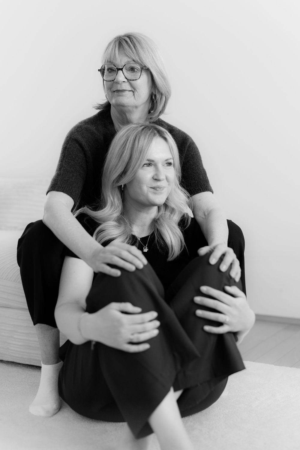 Black and white portrait of two blonde women posing together indoors, wearing dark clothing.