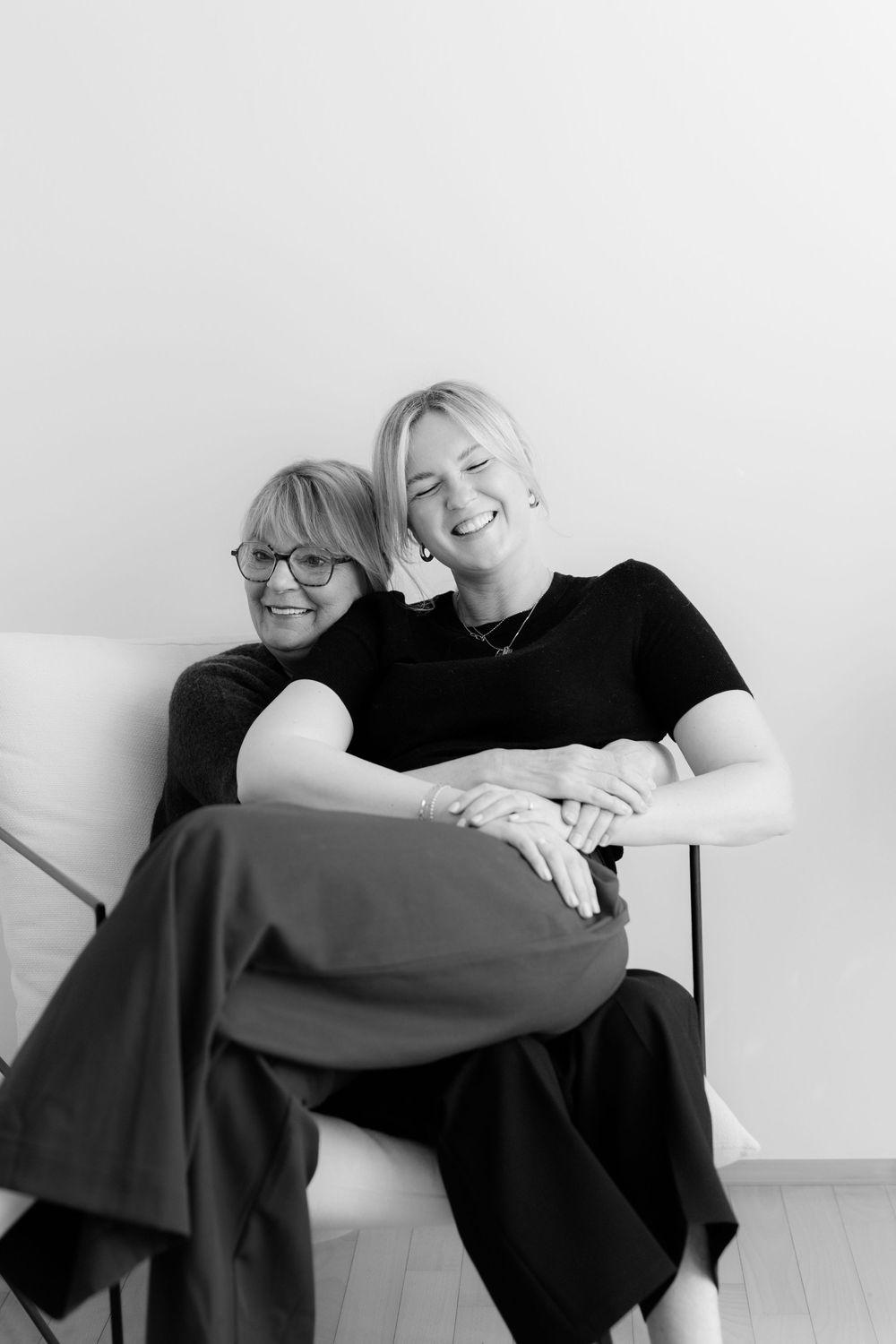 Two women laughing and embracing in a chair, black and white portrait photo.