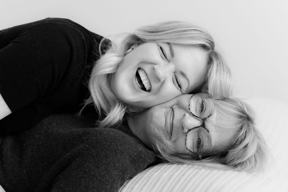 Two blonde women laughing joyfully together in a black and white portrait photo.