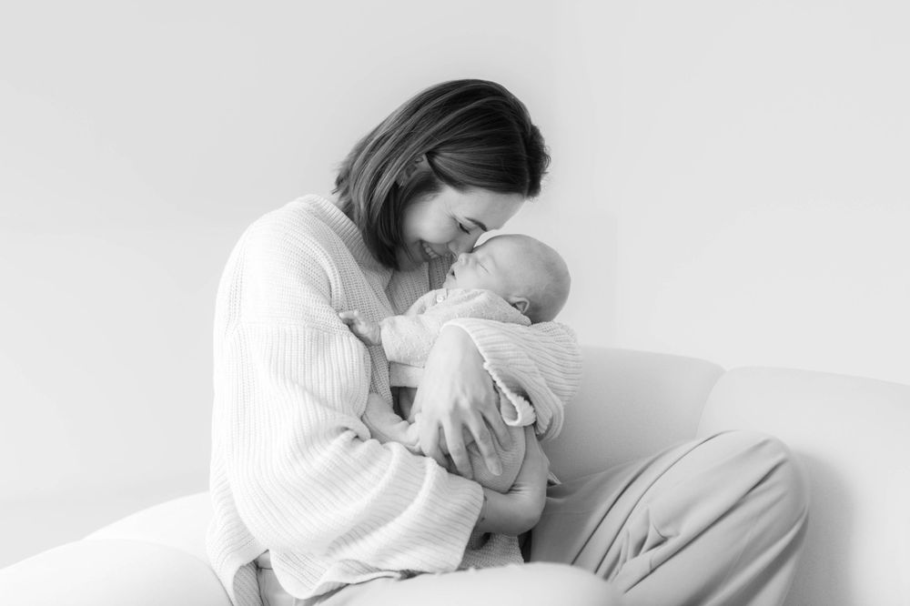 Black and white photo of a mother tenderly holding and nuzzling her newborn baby while seated.