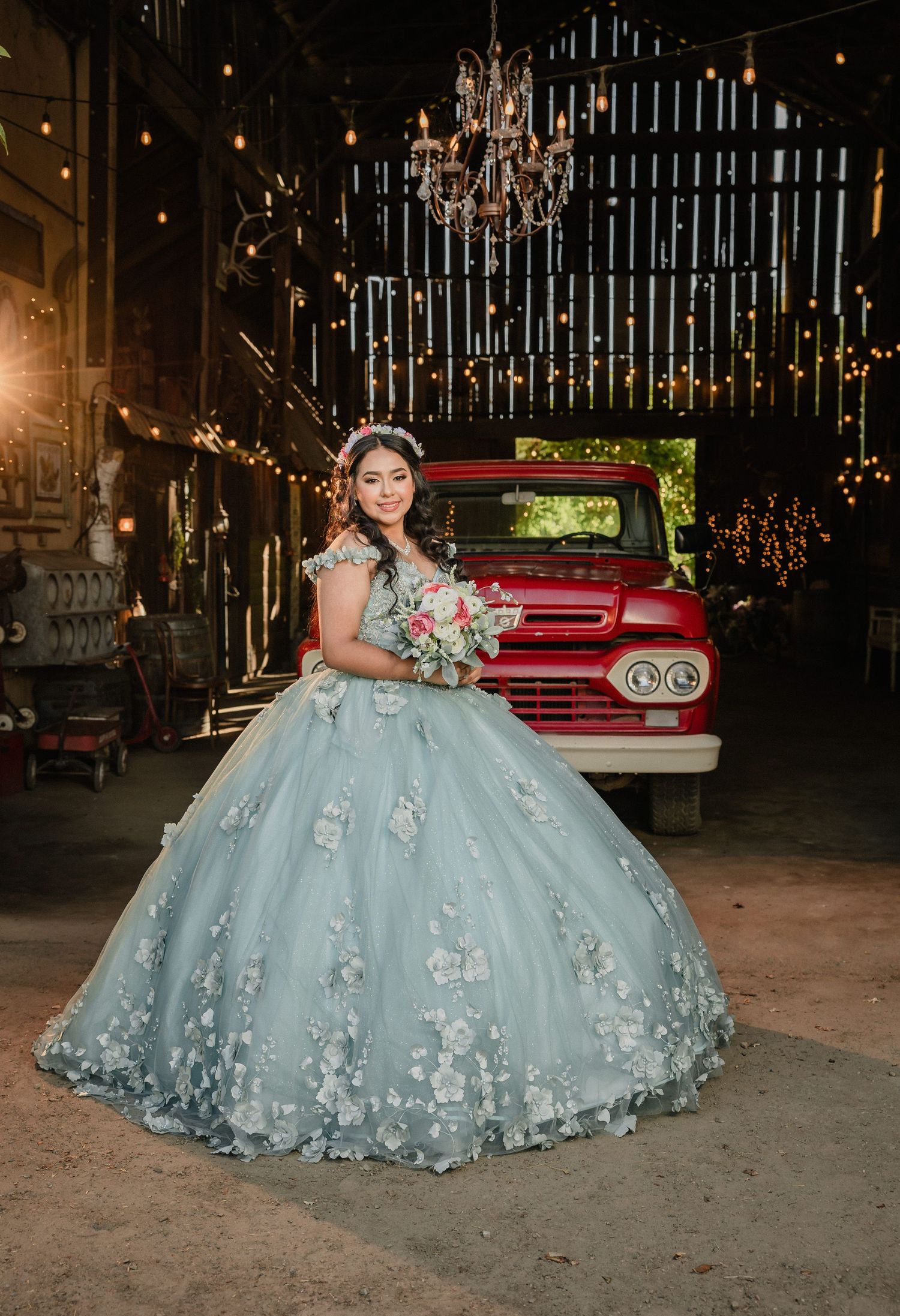 Woman in blue ball gown poses by a pond in front of a white castle-like mansion on a sunny day.
