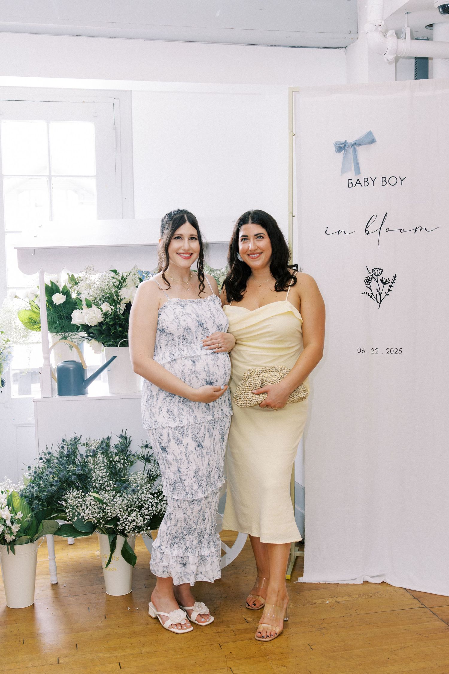Pregnant woman at baby shower with friends touching her belly, blue balloon arch backdrop.
