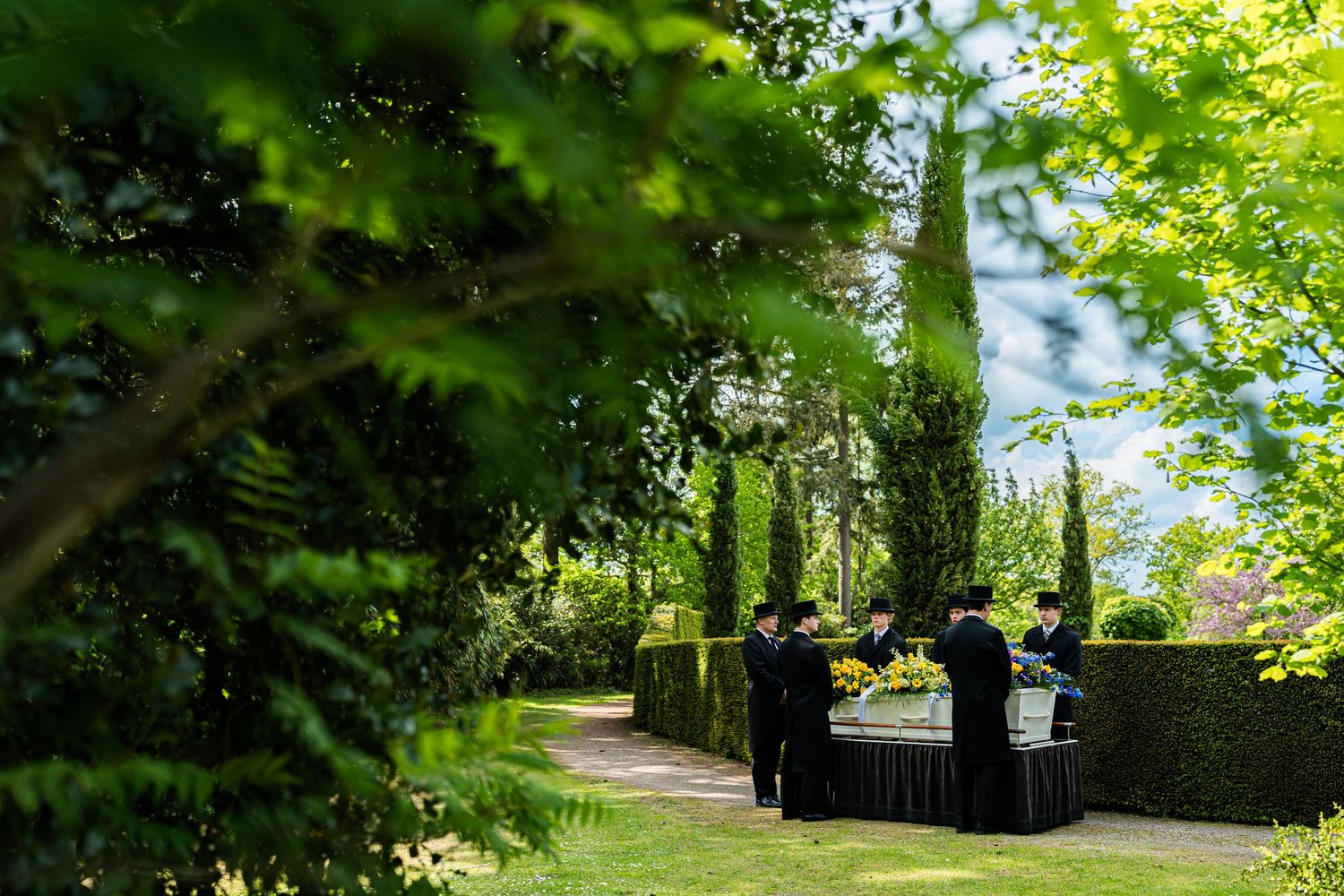 Elegantly dressed staff serving guests in a lush green garden with manicured hedges and tall trees.