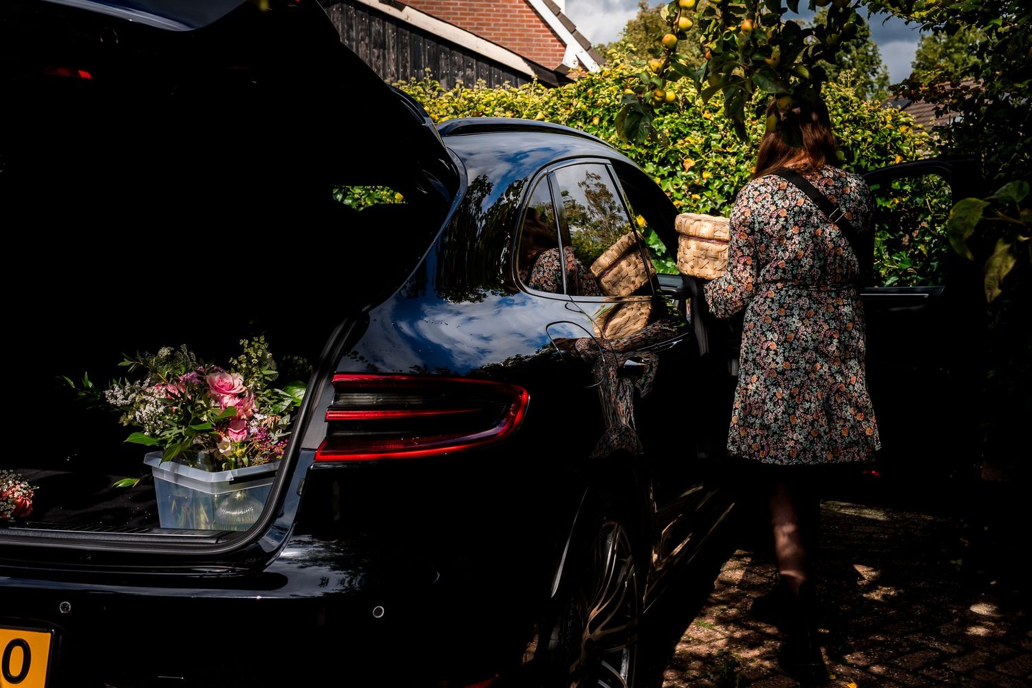 Woman loading floral arrangements into a black car trunk outdoors on a sunny day.