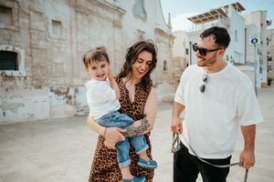 Happy young family with toddler exploring a charming white stone European village street.