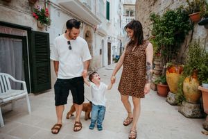 Joyful family of three swinging toddler by hands while strolling a picturesque Italian alley.