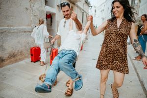 Couple dancing joyfully on a cobblestone street, woman in leopard print dress holding hands with man in white shirt and jeans.