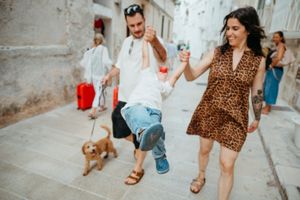 Family swinging child between them while walking dog on cobblestone street in European town.