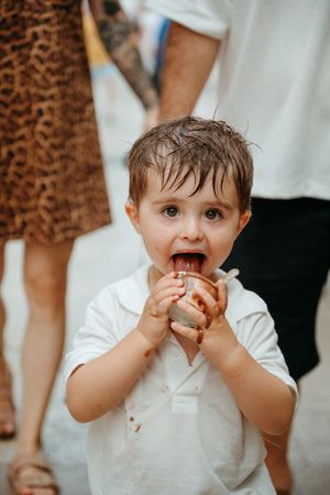 Adorable toddler in white shirt eating chocolate ice cream with messy face outdoors.