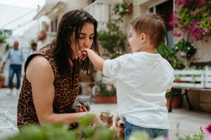 Young mother in leopard print dress receives food from her toddler son in a charming outdoor setting.