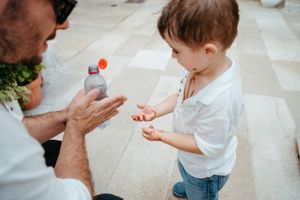 Father uses hand sanitizer with his young toddler son on a sunny outdoor patio.