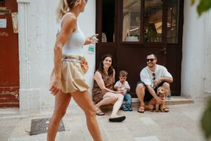 Family with toddler and golden dog sitting outside a European cafe while a woman walks by.