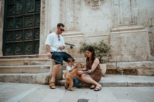 A family with a toddler and golden doodle dog sitting on stone steps outside a historic building.