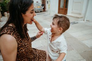 Happy mother in leopard dress sharing ice cream with her messy-faced toddler son outdoors.
