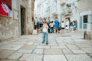 Young child standing alone in a historic European cobblestone street with tourists in background.
