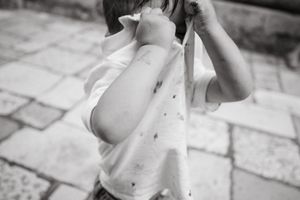 Black and white photo of young child in dotted shirt wiping face with shirt hem.